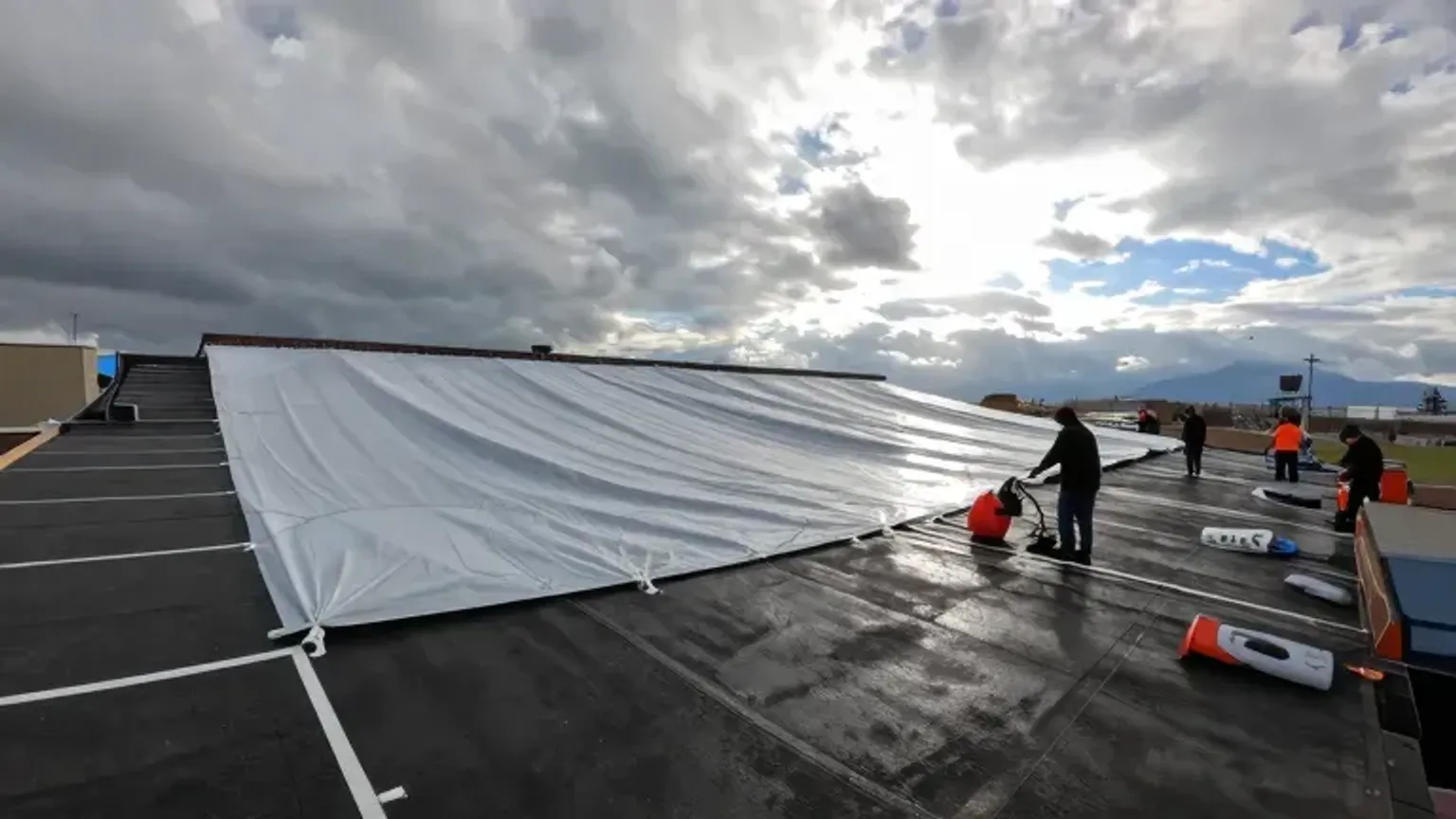 Documentary-style iPhone photo of emergency commercial roof tarping and temporary weatherproofing after storm damage in Saratoga Springs, Utah. Natural lighting.