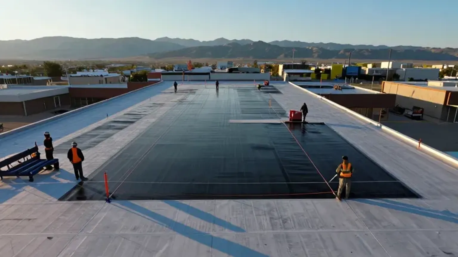 Documentary-style iPhone photo of commercial flat roofing installation in Saratoga Springs, Utah with crew applying membrane system. Natural daylight.