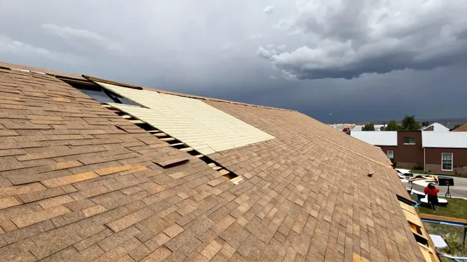 Documentary-style iPhone photo of storm-damaged roof repair in Saratoga Springs, Utah with missing shingles being replaced. Natural daylight.